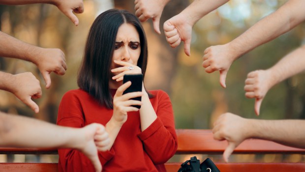 Kobieta patrzy na telefon, jest smutna, otrzymuje negatywne komentarze i hejt