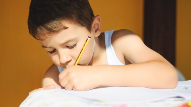 Chłopiec odrabia lekcje, pisząc lewą ręką