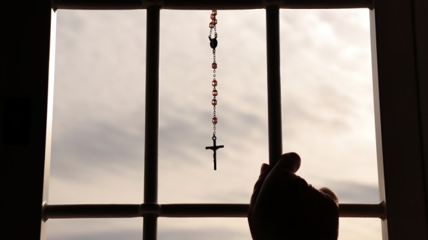 Religious rosary hanging on window with grate