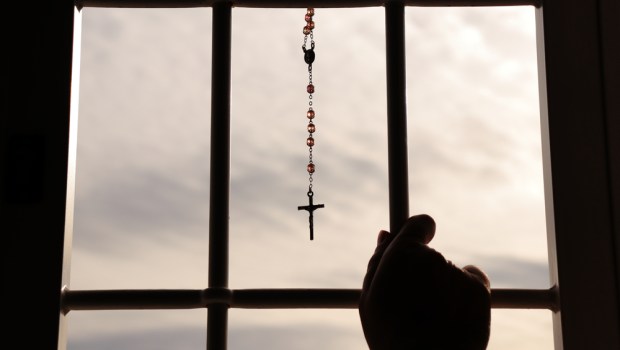 Religious rosary hanging on window with grate