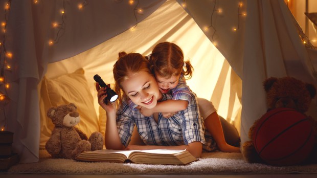 mama z córką czytają książkę pod namiotem z koca oświetlając ją latarką