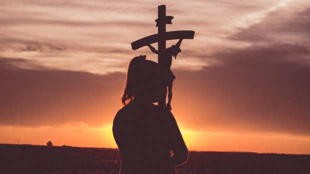 dziewczyna przytula krzyż o zachodzie słońca