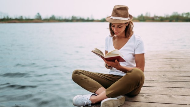 kobieta odpoczywa nad jeziorem i czyta książkę