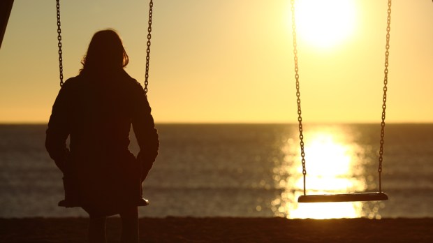 samotna kobieta siedzi na huśtawce i patrzy w morze o zachodzie słońca