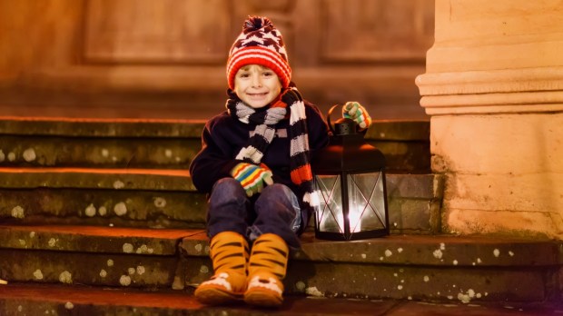 chłopiec siedzi na schodach przed kościołem i trzyma lampion adwentowy