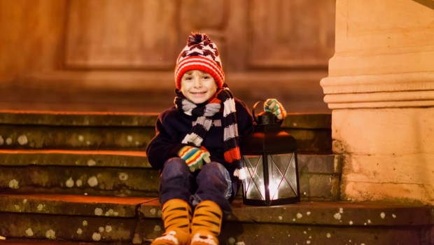 chłopiec siedzi na schodach przed kościołem i trzyma lampion adwentowy