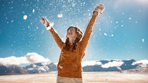 Rozradowana kobieta w wysokich górach podrzuca do góry śnieg