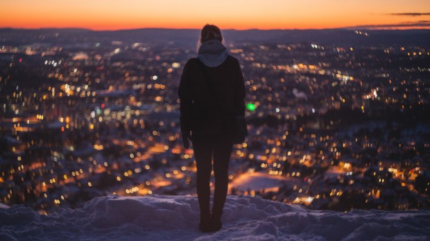 kobieta stoi wysoko w śniegu i patrzy na panoramę miasta u podnóża góry o wschodzie słońca