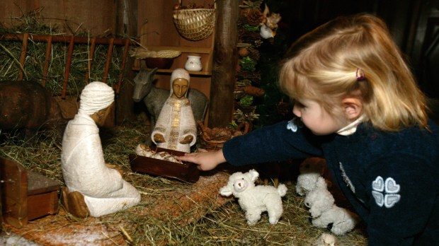 mała dziewczynka sięga rączką do szopki i dotyka figurki małego Jezusa