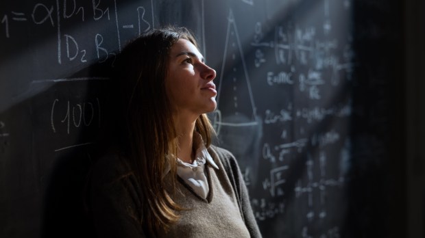 Zamyślona studentka matematyki przed tablicą zapisaną wzorami matematycznymi i fizycznymi