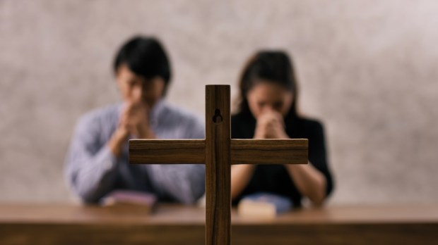 para wiernych modli się w kościele przed krzyżem za kogoś
