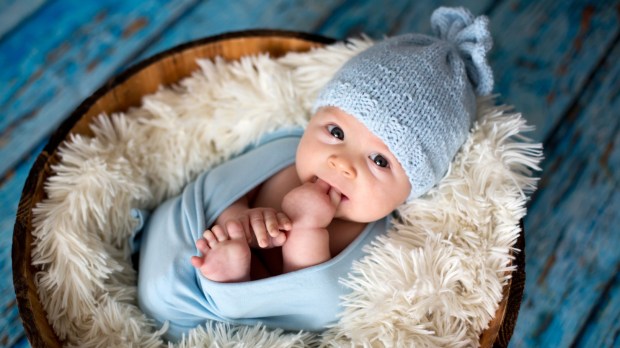 noworodek leży w kosztu, ubrany w niebieską czapkę i pieluszkę