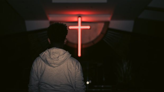 young man looks at red neon cross