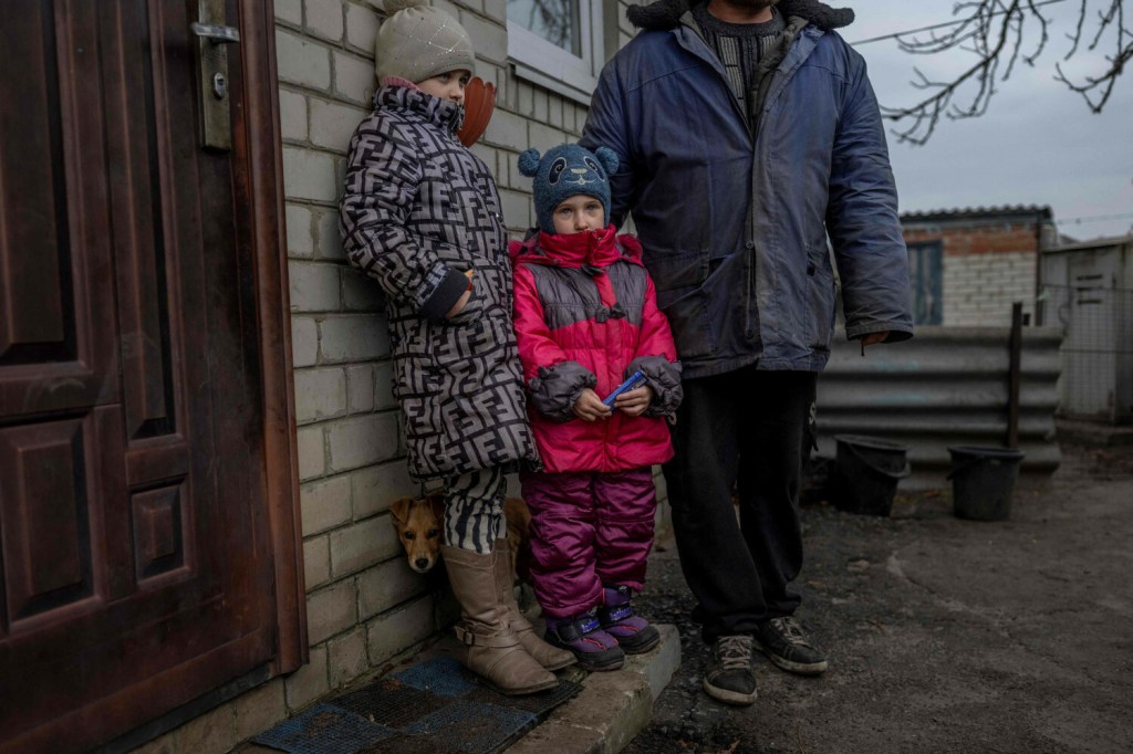 Dzieci z Ukrainy stoją ze swoim ojcem przed domem we wsi Zariczne w pobliżu linii frontu (10 listopada 2022)