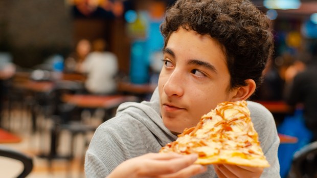 nastolatek je pizzę ze znajomymi w pizzerii i słucha ich rozmowy