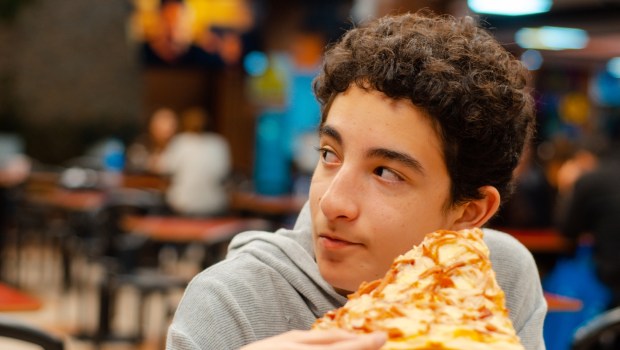 nastolatek je pizzę ze znajomymi w pizzerii i słucha ich rozmowy