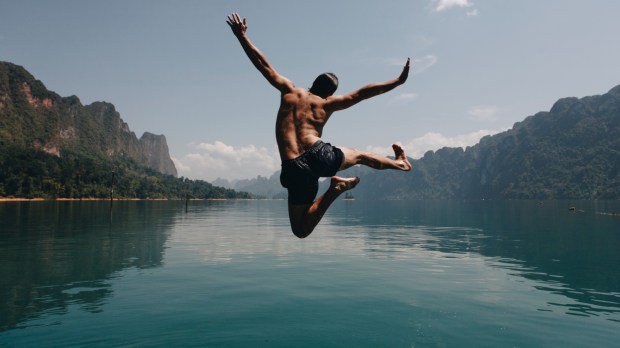 Mężczyzna skacze z radością do górskiego jeziora