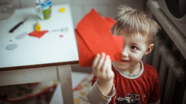 Mały chłopiec pokazuje rodzicom podartą czerwoną kartkę papieru