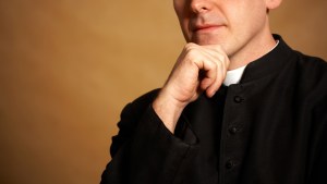 Ksiądz katolicki zastanawia się nad czymś, podpierając ręką brodę
