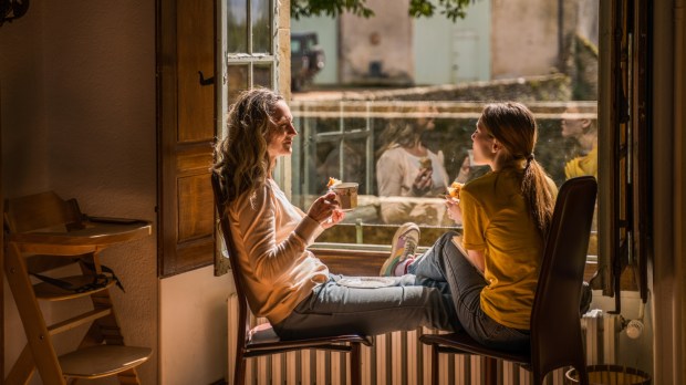 Matka z nastoletnią córką siedzą w mieszkaniu przy oknie i piją herbatę