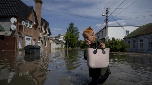 Mieszkanka Chersonia przedziera się przez drogę zalaną wodami Dniepru w wyniku uszkodzenia tamy w Nowej Kachowce