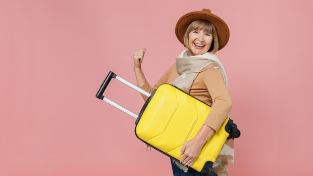 Zadowolona kobieta w średnim wieku z walizką podróżną w ręce