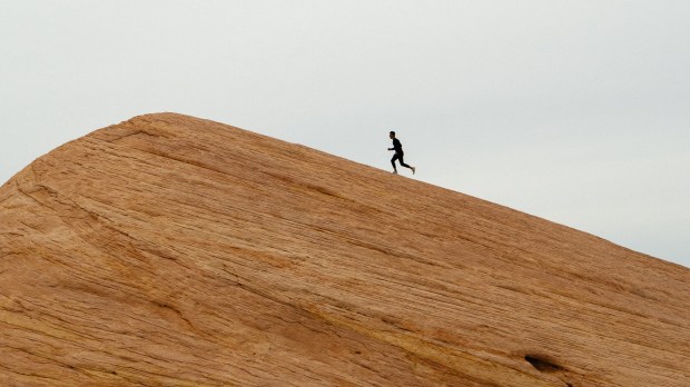 Mężczyzna wbiega na szczyt pustynnej wydmy
