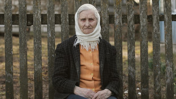 Staruszka siedząca na ławeczce przy płocie na polskiej wsi