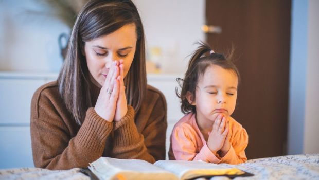 Matka i córką klęczą przy łóżku i modlą się nad otwartą Biblią