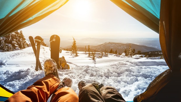 Para narciarzy odpoczywa w namiocie. Ich narty i snowboard leżą przed nimi wbite w śnieg
